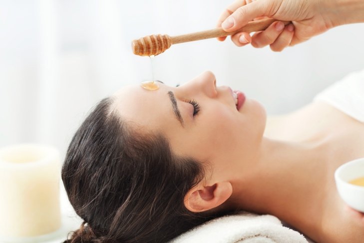 Woman waits patiently as a hand pours honey onto her face for a face mask